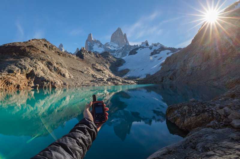 Person with arm extended holding a Garmin inReach Mini overlooking an alpine lake