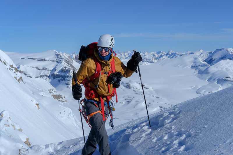 Packup co-founder Taylor Burk donning a climbing harness and camera while approaching a wintry summit