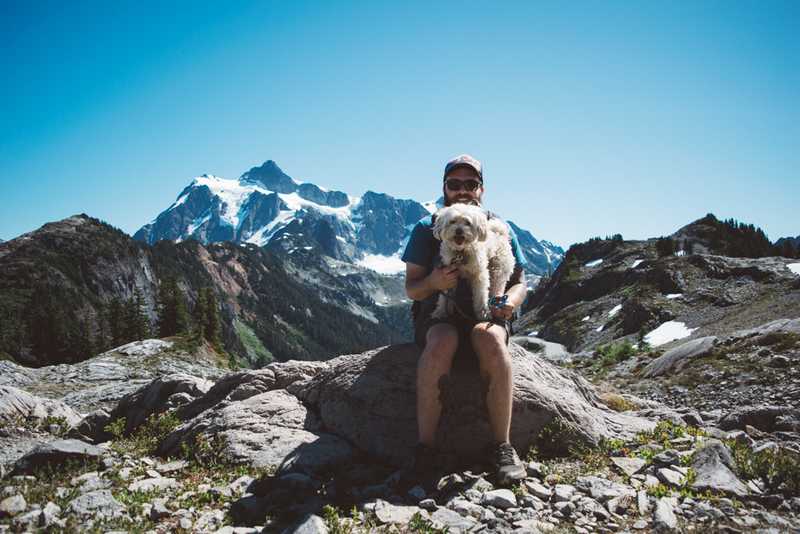 Packup co-founder Tony Mamo and his dog sitting on a pile of rocks with Mt Shuksan in the background